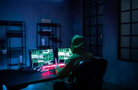 This image shows a hacker man working on computers alone in dark room, rear view. 