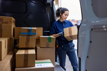 This image shows a woman unloading packages from a box truck. Last mile delivery businesses continue to face a truck driver shortage, because many offer low pay and no benefits. This blog post discusses potential solutions.