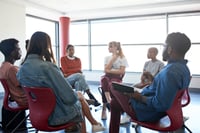 The image displays a group of diverse college students sitting in a circle, discussing mental health and seeking support during the summer break. 