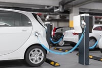 The photo shows an electric car charging in a garage with a focus on environmental risks and insurance implications. 