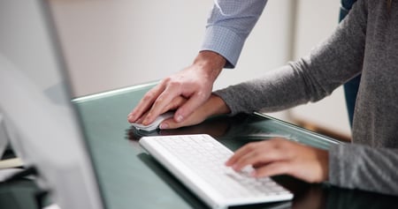 This photo shows the arms and hands of a female employee wearing a lightweight grey sweater. Her left hand rests on a slim, white, standalone keyboard. Her right hand is on a computer mouse, and on top of that hand rests the right hand of a male colleague. The touching feels inappropriate for a workplace. The New York Adult Survivors Act (ASA) allows people to file suit for workplace sexual offenses like this, even if the statute of limitations has expired. But the look mechanism closes on November 24, 2023. 