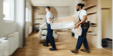 Two professional movers delivering furniture inside of a home