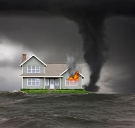 A house is on fire in the middle of a flood. It’s a two-story, single-family home with a faded blue exterior and light grey roof. Flames are engulfing a portion of the house, and smoke is billowing into the sky. Water has deluged the surrounding area leaving the house practically floating. The brown and murky floodwaters portray a scene of despair. There is even a tornado swirling in the background, threatening to test the final integrity of the house. While the combination of wildfire, flood, and tornado seem like an improbable event, the image highlights the dramatic nature of climate change. This visual represents the impact of the climate crisis on insurance capacity. 
