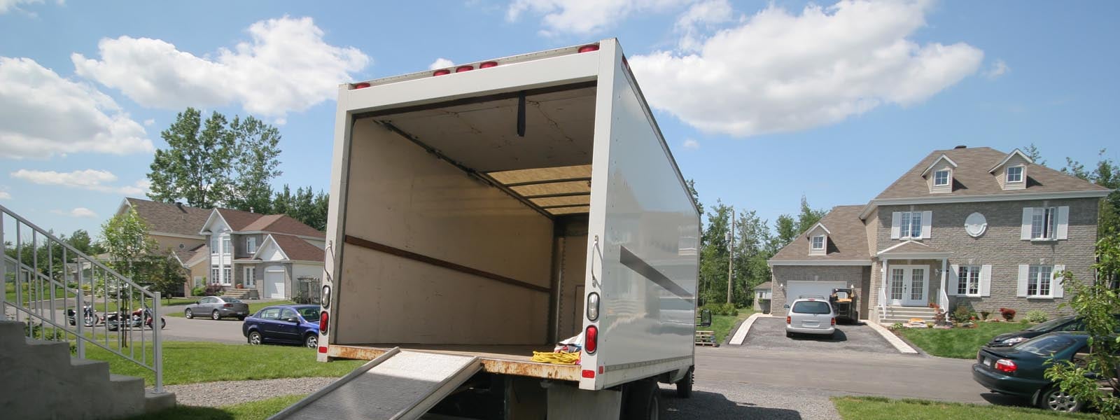 A box truck parking in the driveway of a home located in a residential neighborhood. The box door is open and a ramp is pulled out for movers to use during an over-the-threshold delivery .