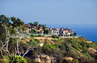 A a row of colorful houses built on a cliff overlooking the ocean in California. The houses appear to be made of wood and painted in bright colors, such as red, yellow, and blue. They have balconies with glass windows facing the ocean.  Some of the houses have  satellite dishes mounted on their roofs.