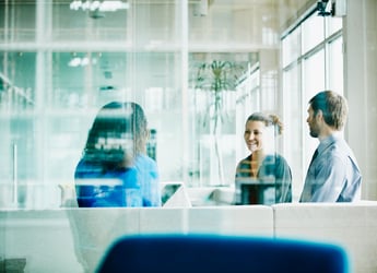 Two professional women discussing benefits enrollment strategy behind a glass office window 