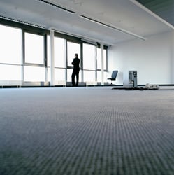 A man is standing next to a set of windows in an office, looking out into the city scape. A desktop computer is sitting in the middle of the room, implying that the business is going through a bankruptcy. Side A policies play a crucial role in protecting individual directors and officers during corporate crises or bankruptcies. 